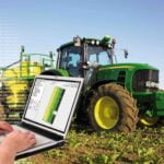 Laptop egy traktor előterében, a képernyőn NEXT Farming Pro látható