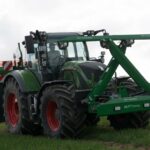 Ein Traktor steht mit einem zusammengeklappten Green Seeker auf einer Wiese.