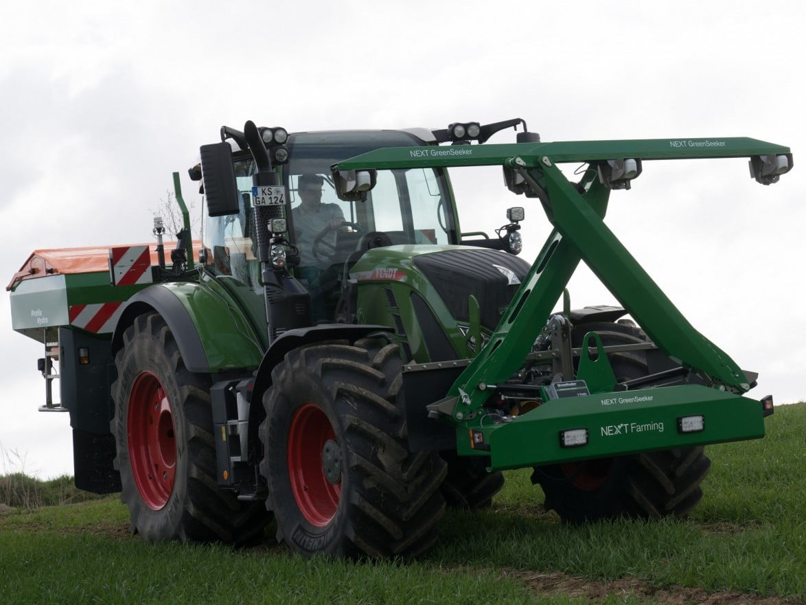 Ein Traktor steht mit einem zusammengeklappten Green Seeker auf einer Wiese.