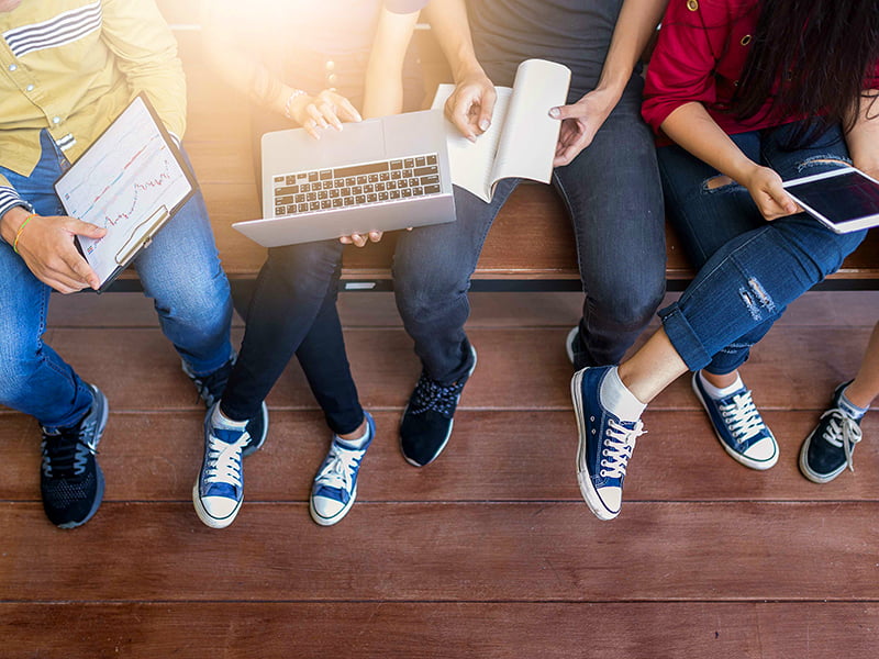 Vier studierende sitzen auf einer Bank mit Laptop