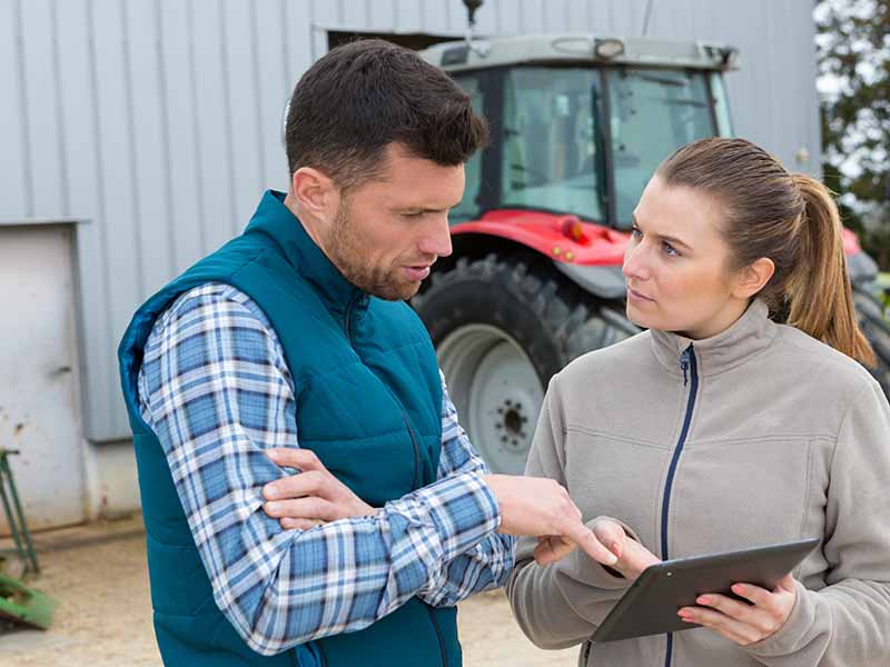 Ein Mann und eine Frau stehen vor einem Traktor und diskutieren über die Verwendung eines Tablets.